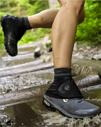A person wearing Topo gaiters running through a stream